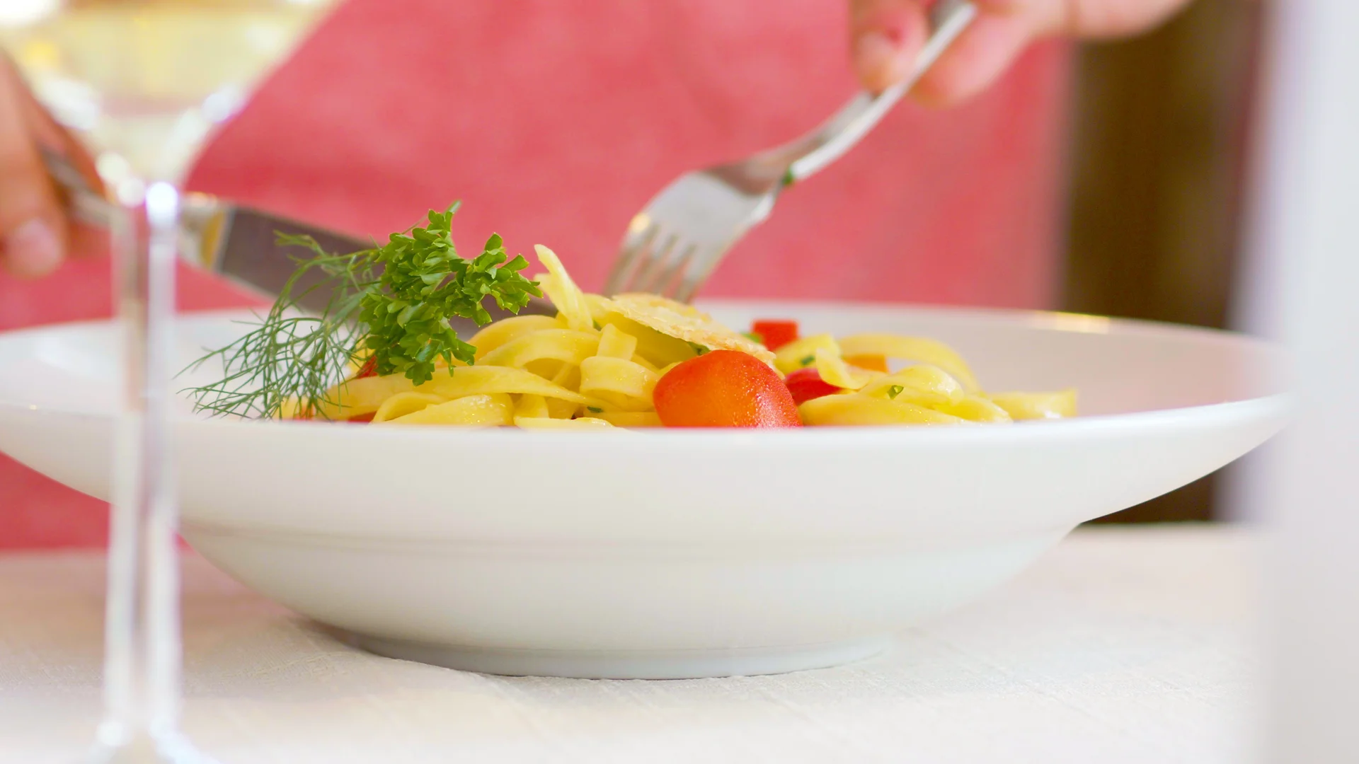 Person isst Pasta mit frischen Kräutern und trinkt Weißwein