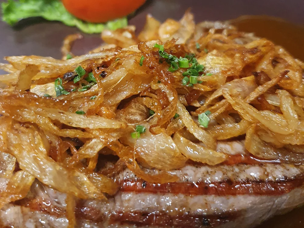 Gegrilltes Steak mit gebratenen Zwiebeln, Salat und Tomate auf einem Teller