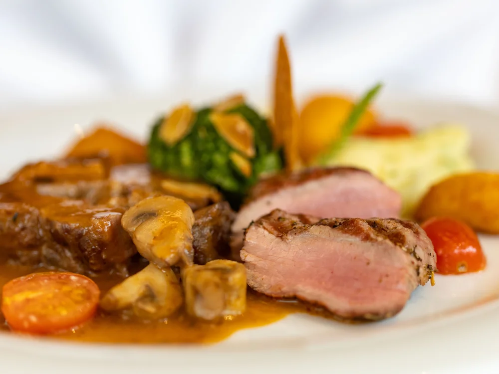 Angerichtetes Fleischgericht mit Pilzen, Tomaten und Kräutern auf Weißem Teller