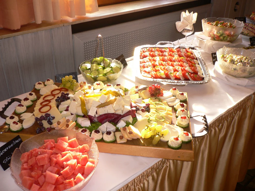 Buffet mit Käse, Wassermelone, Tomaten und Gurkensalat auf weiß gedecktem Tisch