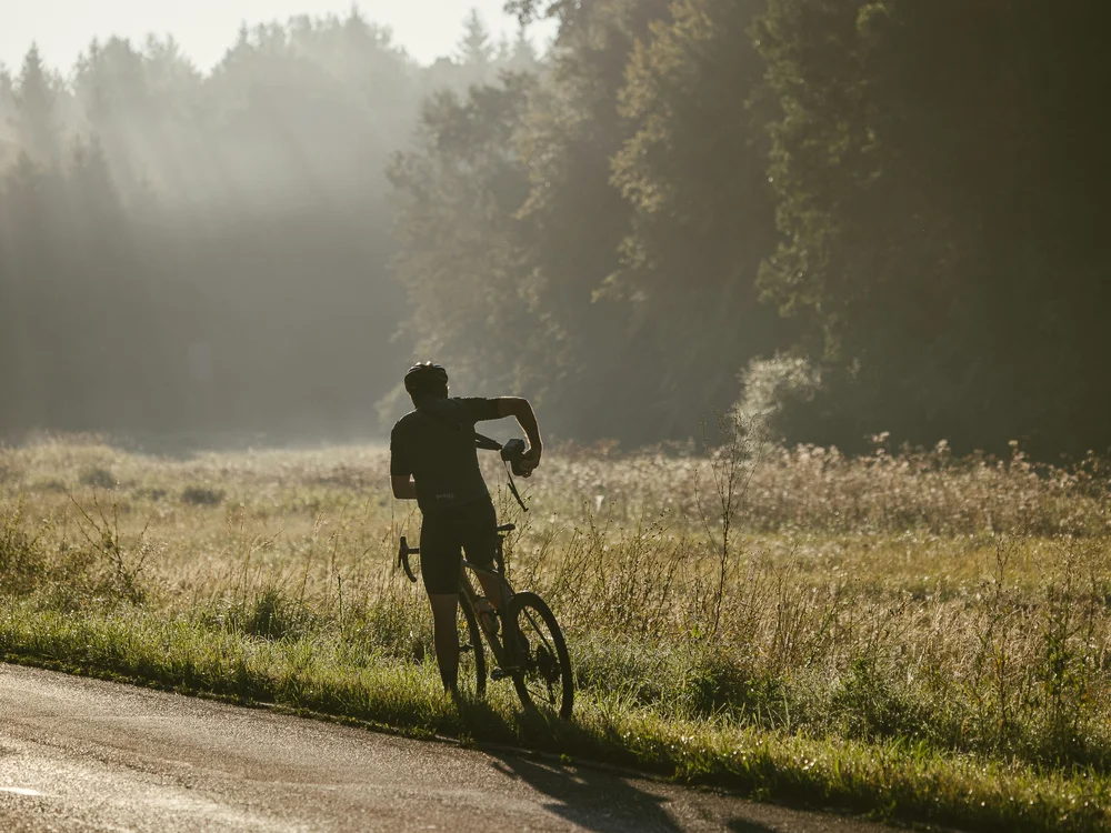 Radfahrer schiebt Fahrrad auf Straße am Morgen mit Sonnenstrahlen im Wald