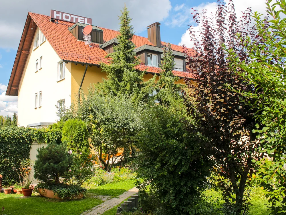 Hotelgebäude mit rotem Dach und grüner Gartenanlage bei Sonnenschein